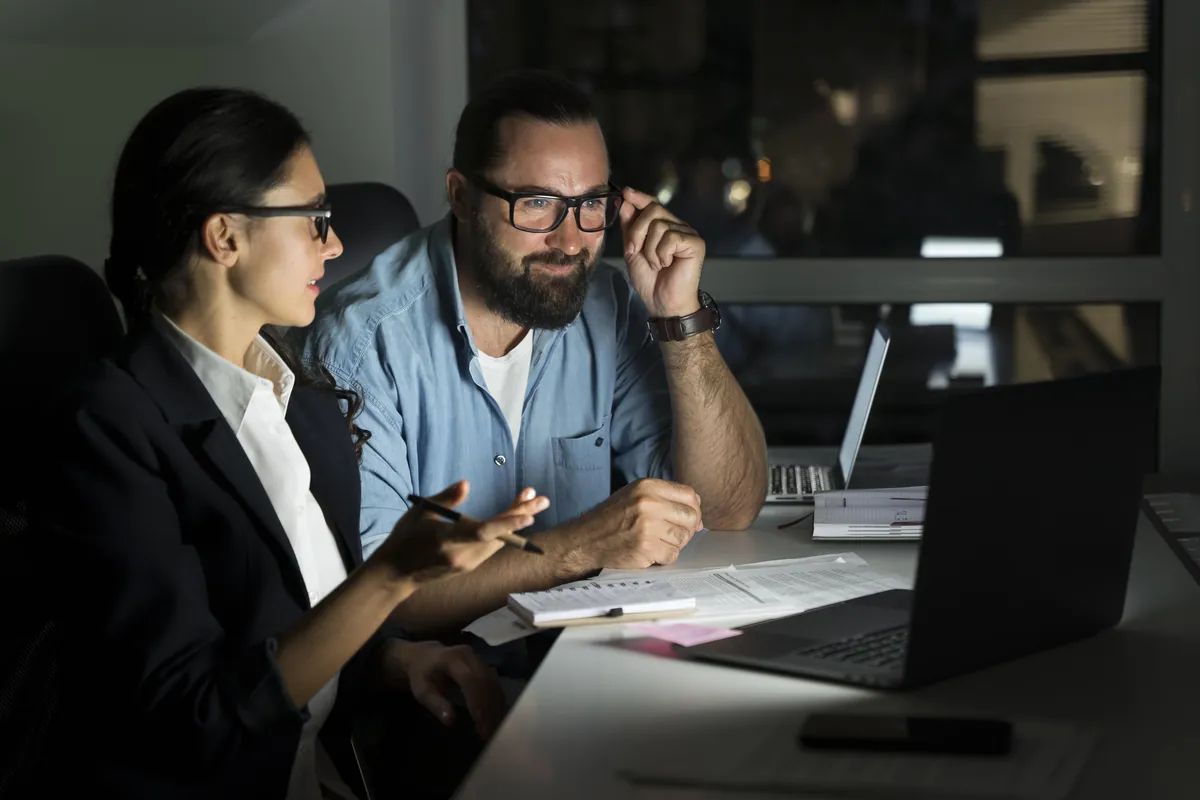 Two professionals working together on a laptop at night