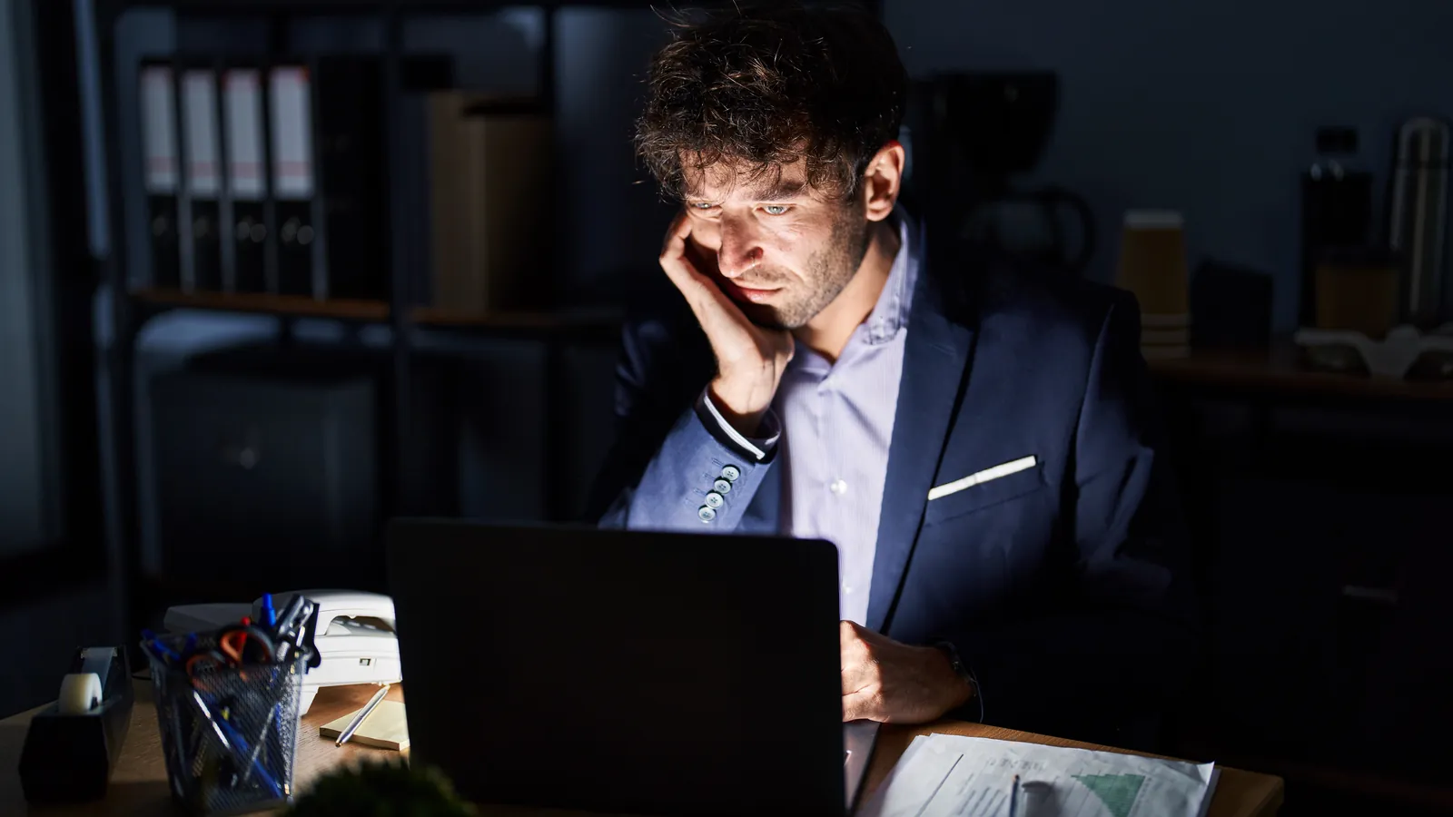 Empresario cansado mirando su computadora portátil en la oficina por la noche