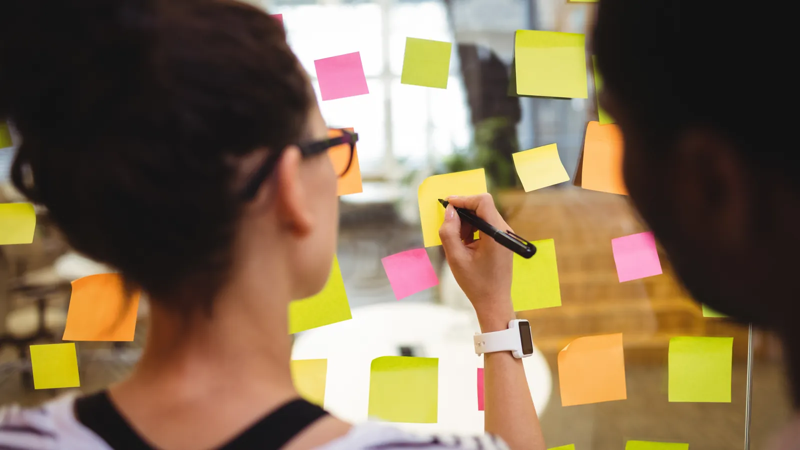 Dos personas organizando notas adhesivas en una pizarra de vidrio durante una sesión de estrategia de marca